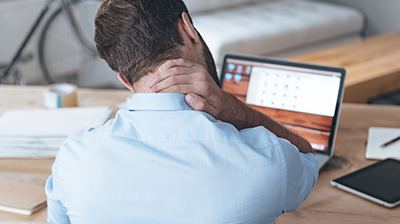 Man sitting at desk stressfully looking down at laptop with hand on his neck.