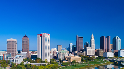 Panoramic image of city skyline on a clear blue day, there are tall buildings and some trees in the background.