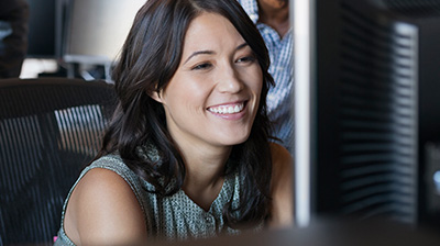 Close up of a woman in business casual attire smiling while looking at a computer monitor.